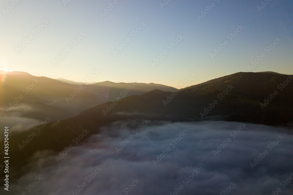 Aerial view of vibrant sunrise over white dense fog with distant dark silhouettes of mountain hills on horizon. Aerial view of vibrant sunrise over white dense fog with distant dark silhouettes of mountain hills on horizon.