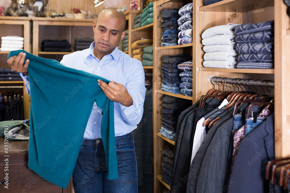 Portrait of young man shopping for clothes choosing sweater in store
