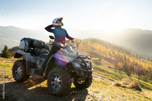 Canvas Print Young happy woman in protective helmet enjoying extreme ride on atv quad motorbike in autumn mountains at sunset