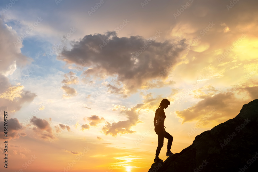Silhouette of a woman hiker climbing up a big stone at sunset in mountains. Female tourist on high rock in evening nature. Tourism, traveling and healthy lifestyle concept.