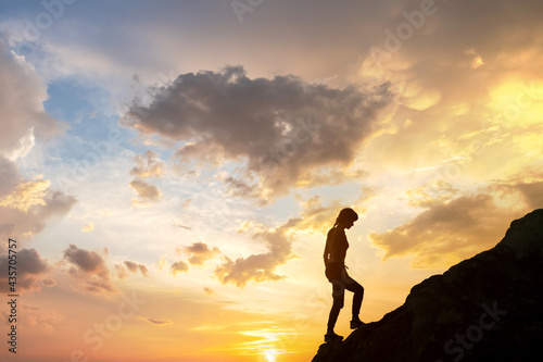 Silhouette of a woman hiker climbing up a big stone at sunset in mountains. Female tourist on high rock in evening nature. Tourism, traveling and healthy lifestyle concept.