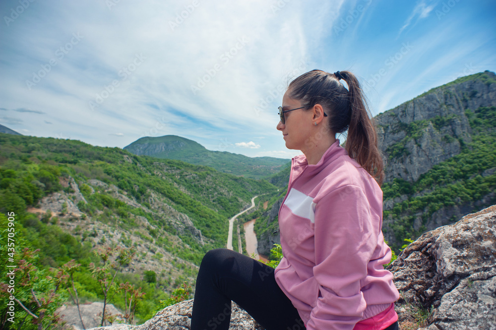 Naklejka premium A young woman is sitting on the top of the canyon in Sicevo (Sićevo, Sićevačka klisura)