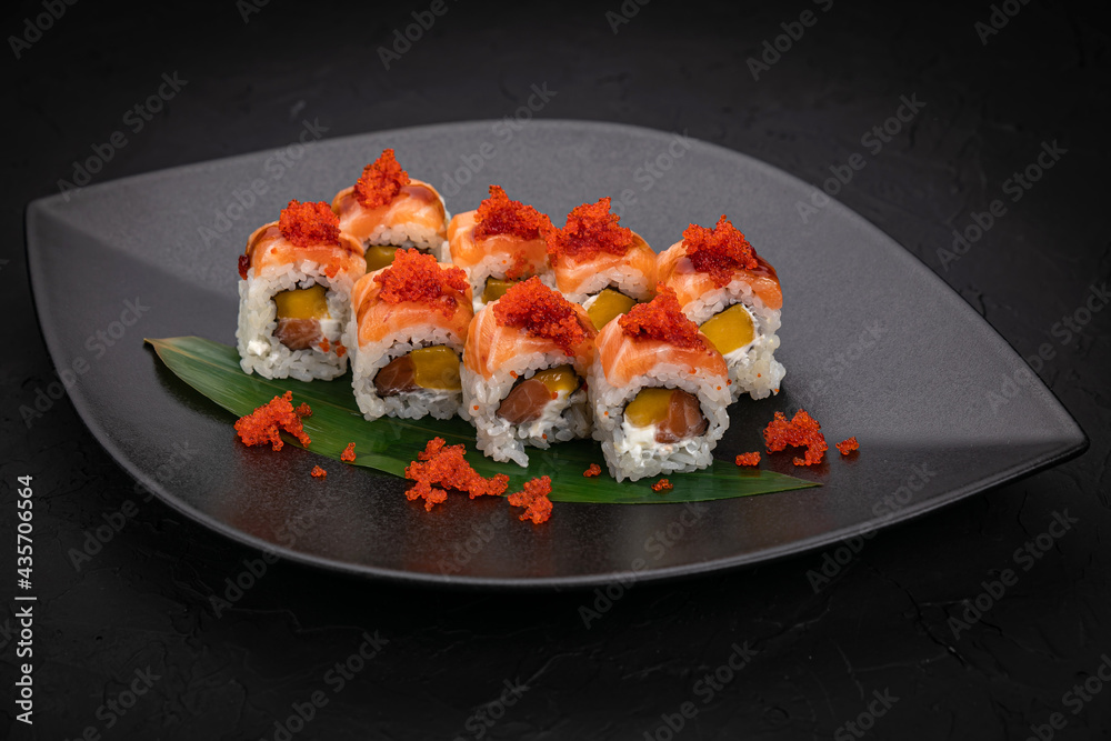 Japanese cuisine. Rolls on a black plate on a wooden table Japanese cuisine. Rolls on a black plate on a wooden table