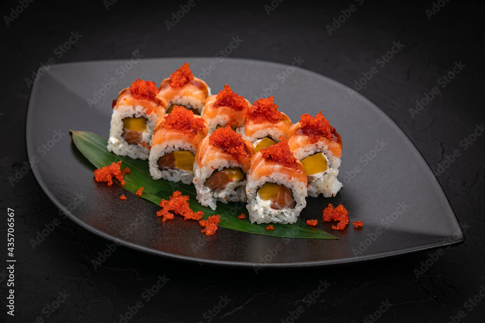 Japanese cuisine. Rolls on a black plate on a wooden table Japanese cuisine. Rolls on a black plate on a wooden table