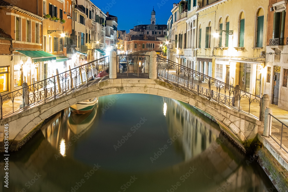 Fototapeta premium Night view of illuminated old architecture, floating boats and light reflections in canals water in Venice, Italy.