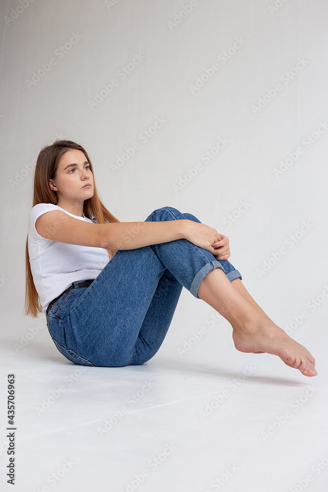 portrait of young attractive caucasian woman with long hair in t-shirt and blue jeans isolated on white background. skinny pretty female sitting on floor at studio. model tests of beautiful lady portrait of young attractive caucasian woman with long hair in t-shirt and blue jeans isolated on white background. skinny pretty female sitting on floor at studio. model tests of beautiful lady