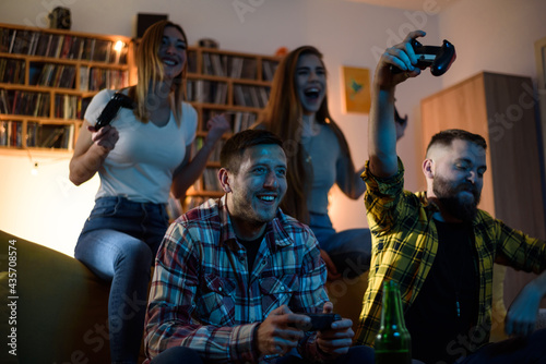 Young fun group of friends playing video games while relaxing at home