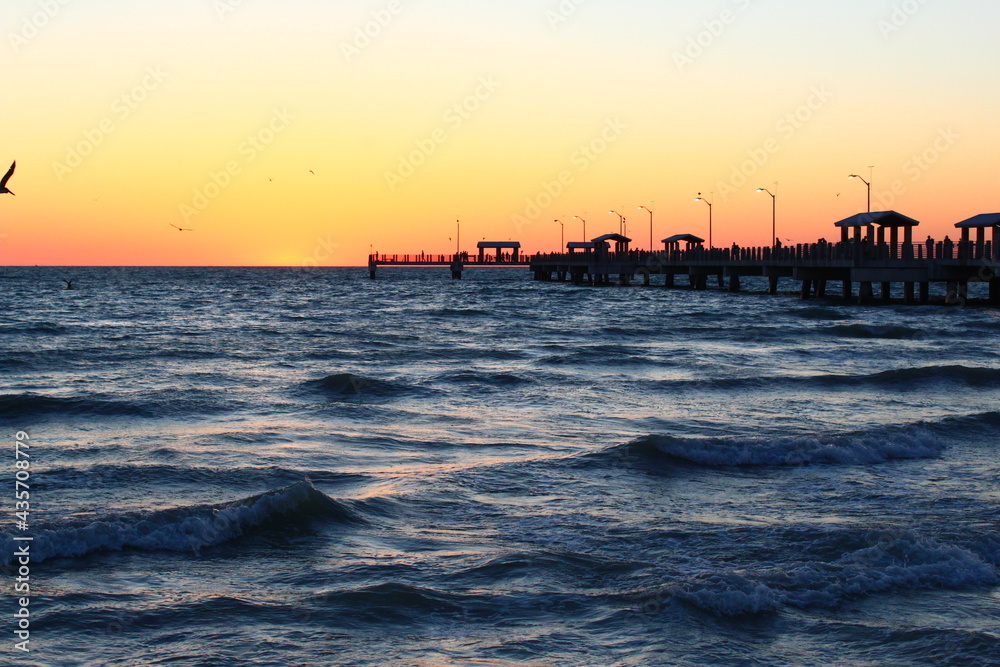 Fishing pier with beach waves with orange glowing sky