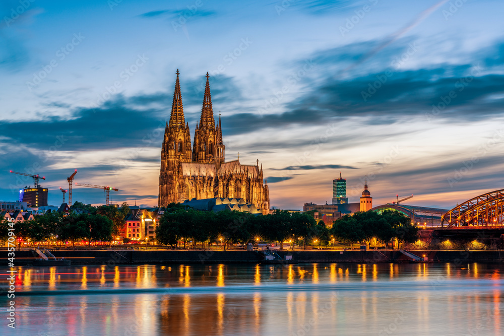 Panoramic view of Cologne Cathedral with Hohenzollern Bridge at nightfall, Germany.