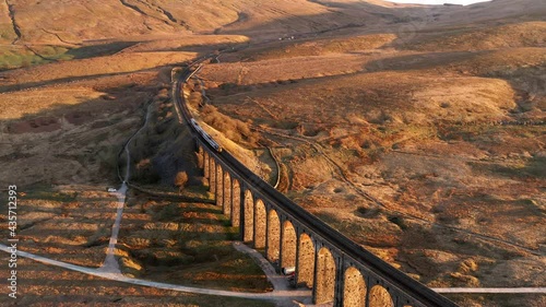 Aerial 4K drone footage showing train crossing over Ribblehead Viaduct in the Yorkshire Dales. Taken in the morning golden hour with stunning warm colours from the rising sun.