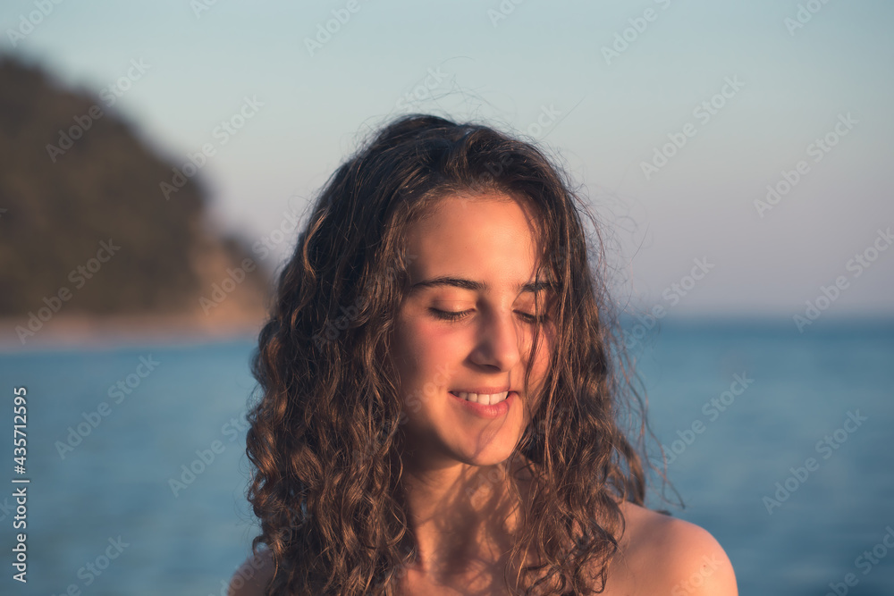Beautiful, young teen girl with curly hair posing by the sea