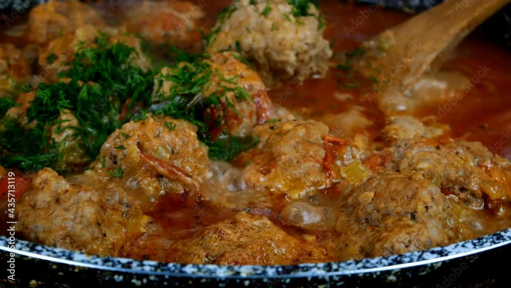 Cooking delicious meatballs in creamy tomato sauce in frying pan. Small round cutlets filled with spicy sauce are stewed in skillet. Domestic kitchen. Close-up. Cooking delicious meatballs in creamy tomato sauce in frying pan. Small round cutlets filled with spicy sauce are stewed in skillet. Domestic kitchen. Close-up.