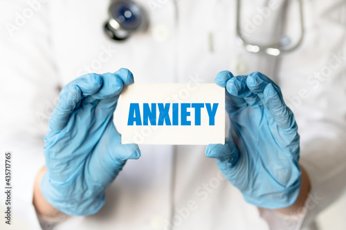 A medical worker in gloves holds a card with the words ANXIETY. Medical concept.