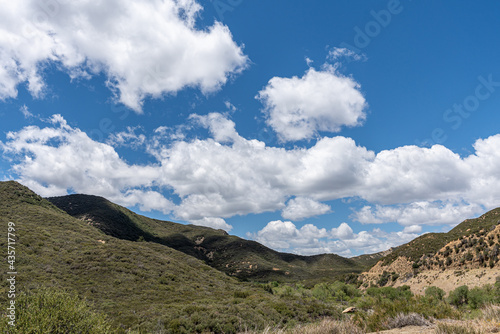 Los Padres National Forest, CA, USA - May 21, 2021: HIgh altitude valley between 2 mountain ranges with green vegetation and beige-brown flanks under blue cloudscape.