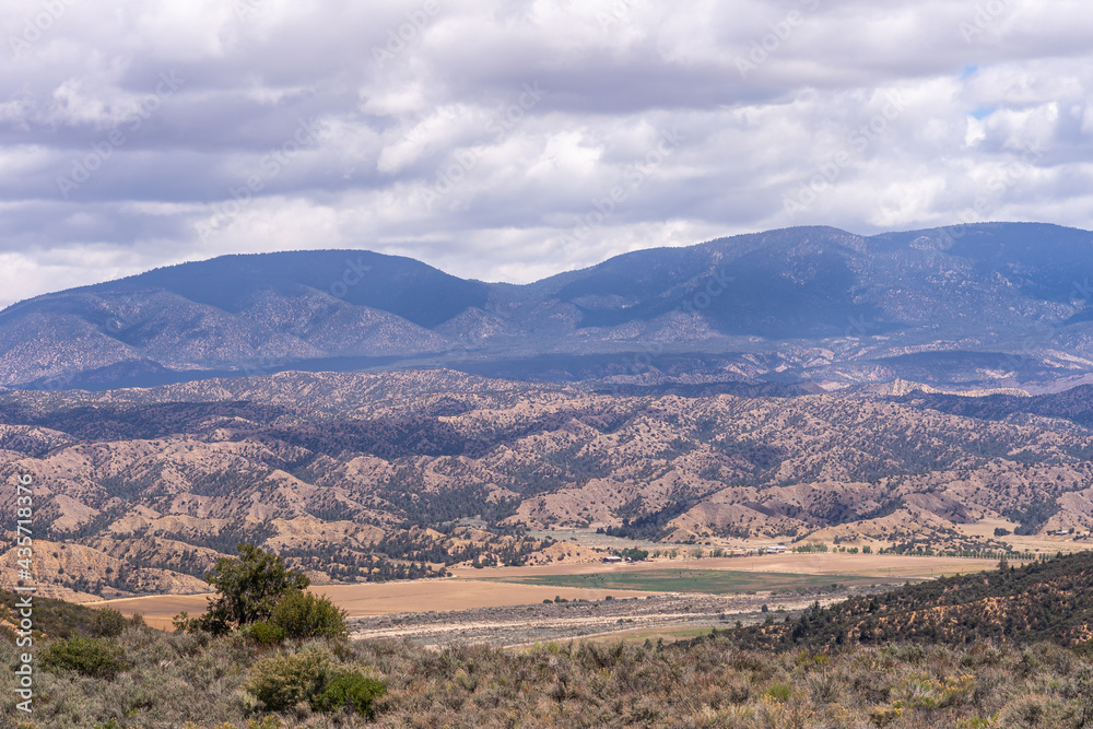 Los Padres National Forest, CA, USA - May 21, 2021: Dry mountain range in eastern part under thick rainy cloudscape with agriculture in valley. Shrub vegetation.