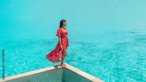 Elegant asian woman relaxing at luxury pool resort overlooking turquoise ocean in red beach coverup maxi dress. Summer sun bikini lifestyle. photo