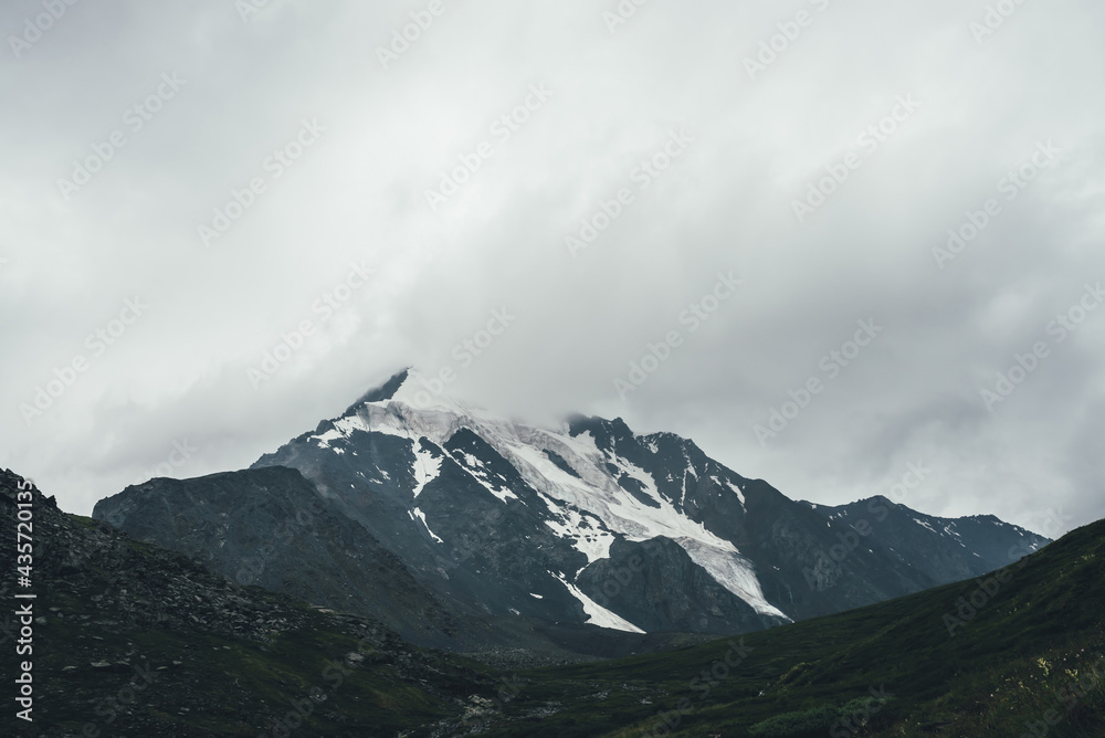 Minimalist monochrome atmospheric mountains landscape with big snowy mountain top in low clouds. Awesome minimal scenery with glacier on rocks. Black white high mountain pinnacle with snow in clouds.