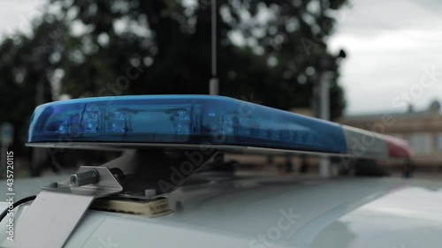 A police officer flashes a light on the roof of a patrol car. The police car flashes red and blue.
