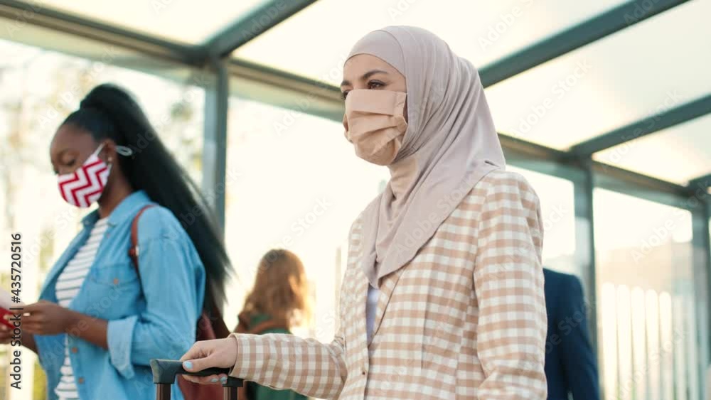 Portrait of mixed-race women with suitcases in masks walking outdoors on street. Different people travelling during coronavirus. Business trip, travels, covid-19 pandemic, safe travel concept Portrait of mixed-race women with suitcases in masks walking outdoors on street. Different people travelling during coronavirus. Business trip, travels, covid-19 pandemic, safe travel concept