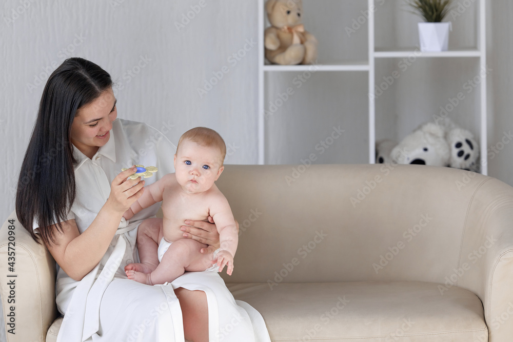 Portrait of a happy young mother embracing her young son. Mom and baby are resting on the couch. Teeth are cut and the child bites the toy. Portrait of a happy young mother embracing her young son. Mom and baby are resting on the couch. Teeth are cut and the child bites the toy.
