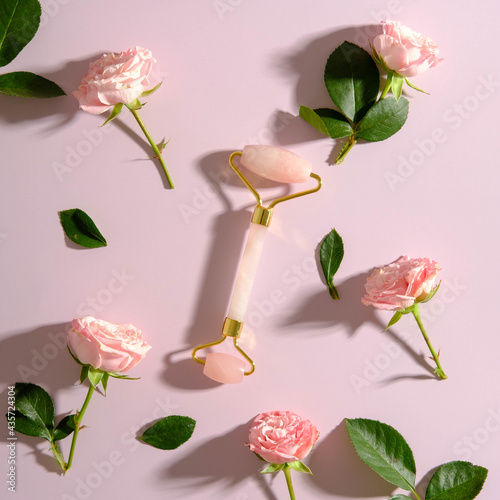 Quartz stone face roller and roses on pink background. Flat lay, top view Facial skincare concept. photo