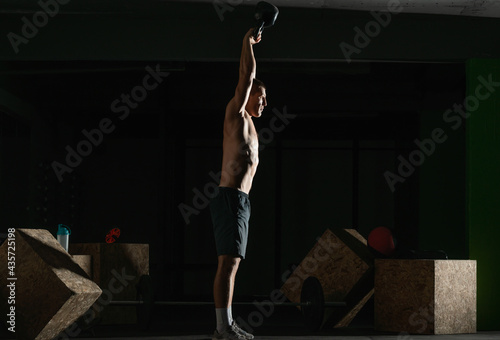 High contrast side view photo of a healthy fitness guy doing workout using a kettlebell