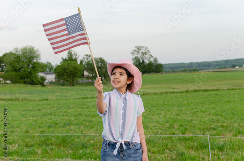 Girl holding American flag with a cowboy hat, celebrating independence day at the farm.
