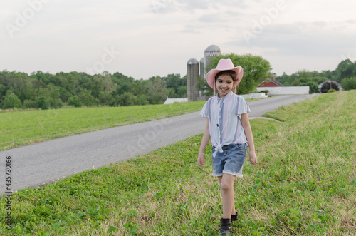 Girl walking on the grass at the farm during the sunset and wearing a pink hat