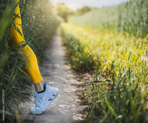 girl runner enters a very thick crop field. she is wearing a yellow leotard and white sneakers. only her leg and the path are visible. trail running. sport and wellness concept.