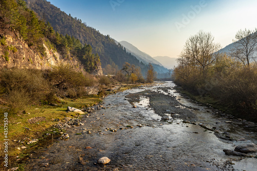 river flowing through misty mountain valley covered with dense forests at dawn from flat angle