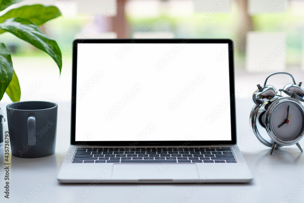 Fototapeta premium Laptop blank white screen with clock coffee mug placed on table. Mock up.
