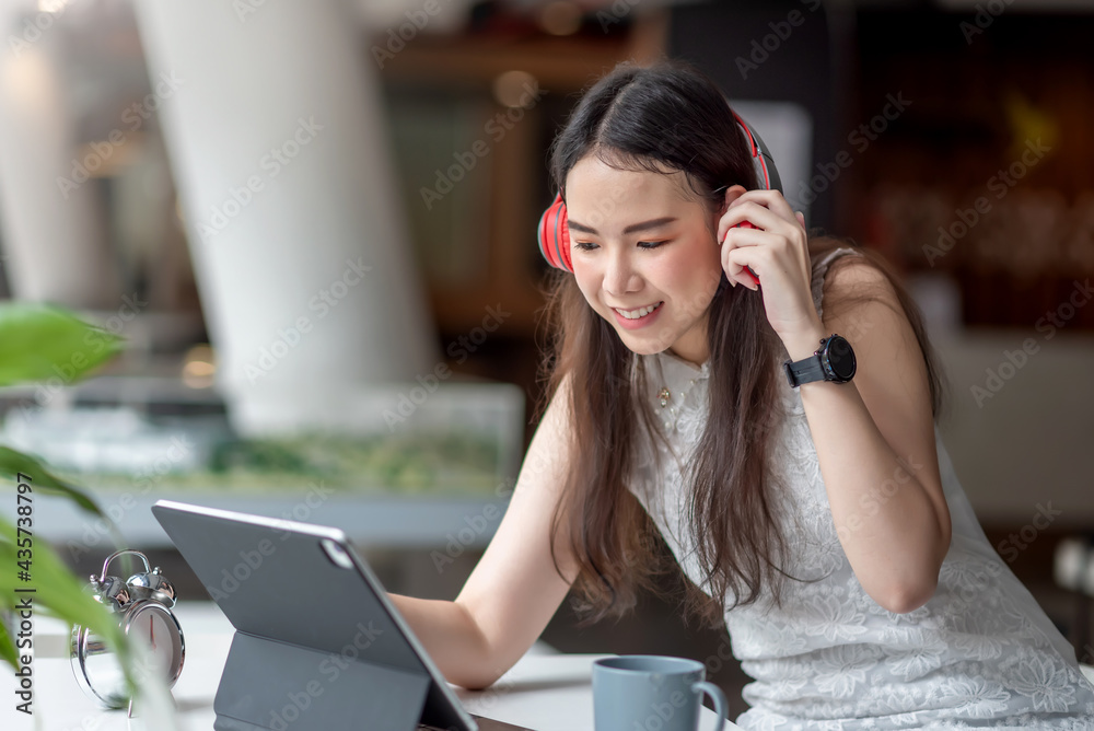 Image of a young Asian woman wearing headphones using a tablet computer at café. Image of a young Asian woman wearing headphones using a tablet computer at café.