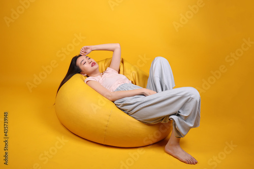 Beautiful young south east Asian woman sits on a yellow beanbag seat orange yellow color background pose fashion style elegant beauty mood expression rest relax think emotion sleep photo