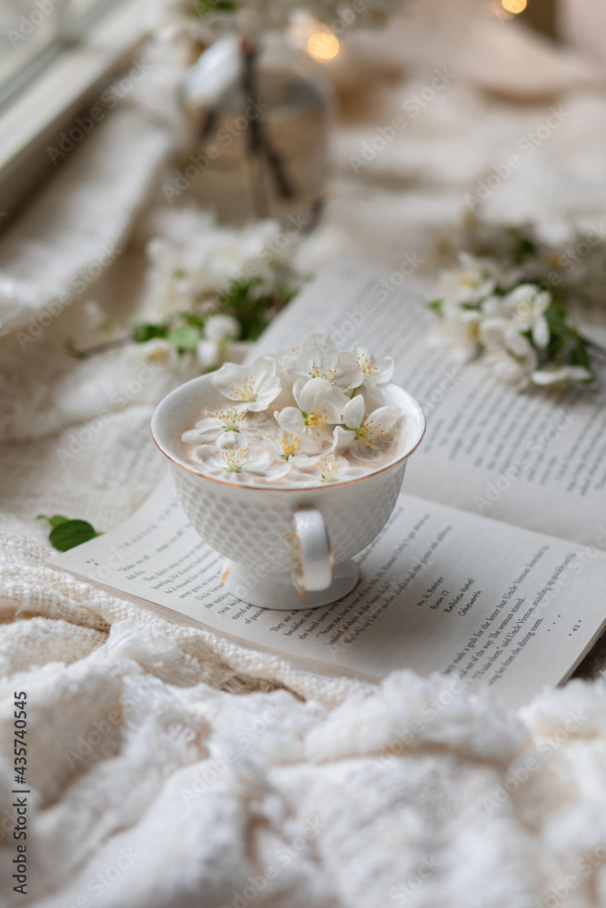 Fresh Spring blossom with a cup of coffee near window with raindrops where sheer curtain and string lights are hanging