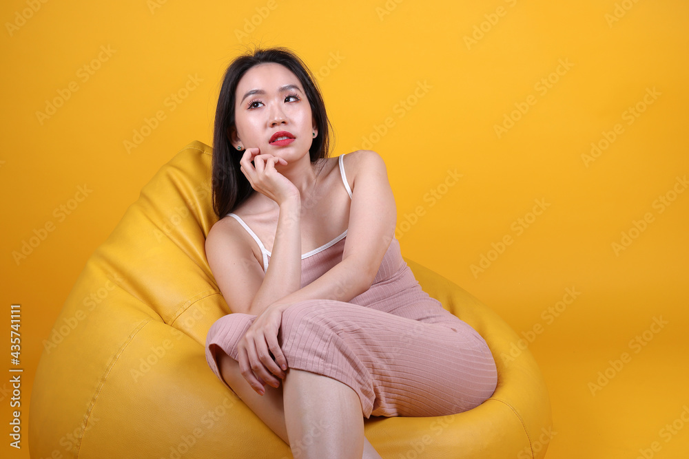 Beautiful young south east Asian woman sit on a yellow orange beanbag seat color background relax rest think emotion imagine expression pose happy wonder Beautiful young south east Asian woman sit on a yellow orange beanbag seat color background relax rest think emotion imagine expression pose happy wonder