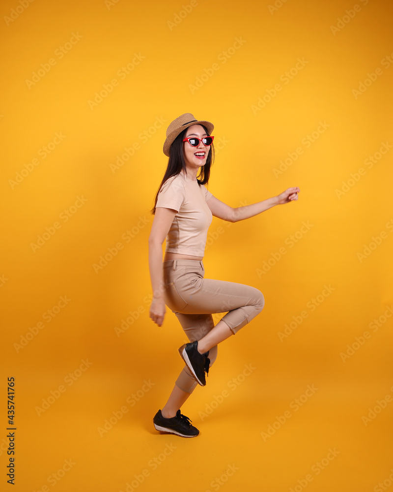 Beautiful young south east Asian woman red frame sunglass hat pose act walk move forward on yellow orange background