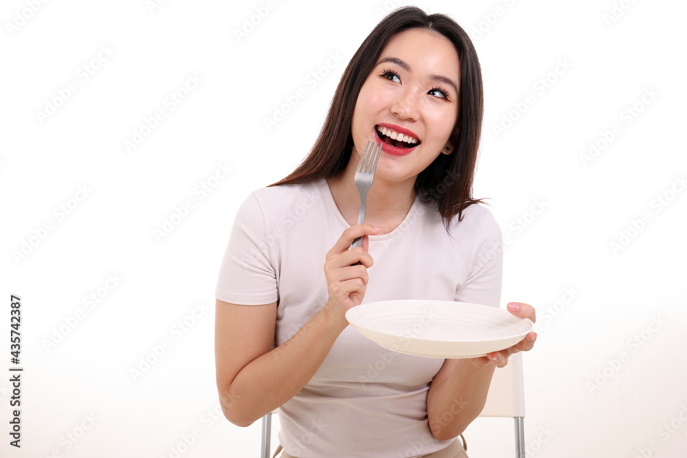 Beautiful young south east Asian woman pretend acting posing holding empty fork spoon white plate in hand eat taste look see white background smile happy food in mouth imagine Beautiful young south east Asian woman pretend acting posing holding empty fork spoon white plate in hand eat taste look see white background smile happy food in mouth imagine