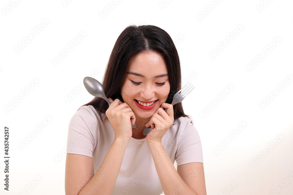Beautiful young south east Asian woman pretend acting posing holding empty fork spoon in hand eat taste look see white plate on table white background smile happy exited Beautiful young south east Asian woman pretend acting posing holding empty fork spoon in hand eat taste look see white plate on table white background smile happy exited
