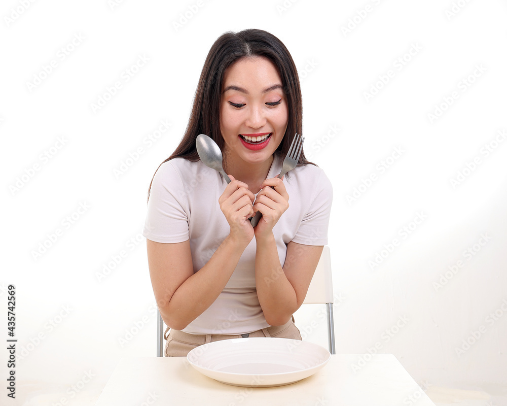 Beautiful young south east Asian woman pretend acting posing holding empty fork spoon in hand eat taste look see white plate on table white background smile happy exited Beautiful young south east Asian woman pretend acting posing holding empty fork spoon in hand eat taste look see white plate on table white background smile happy exited