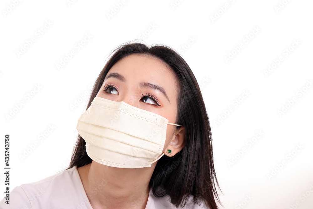 Beautiful young south east Asian woman wearing yellow off white three ply anti virus surgical face mask on white background look up Beautiful young south east Asian woman wearing yellow off white three ply anti virus surgical face mask on white background look up