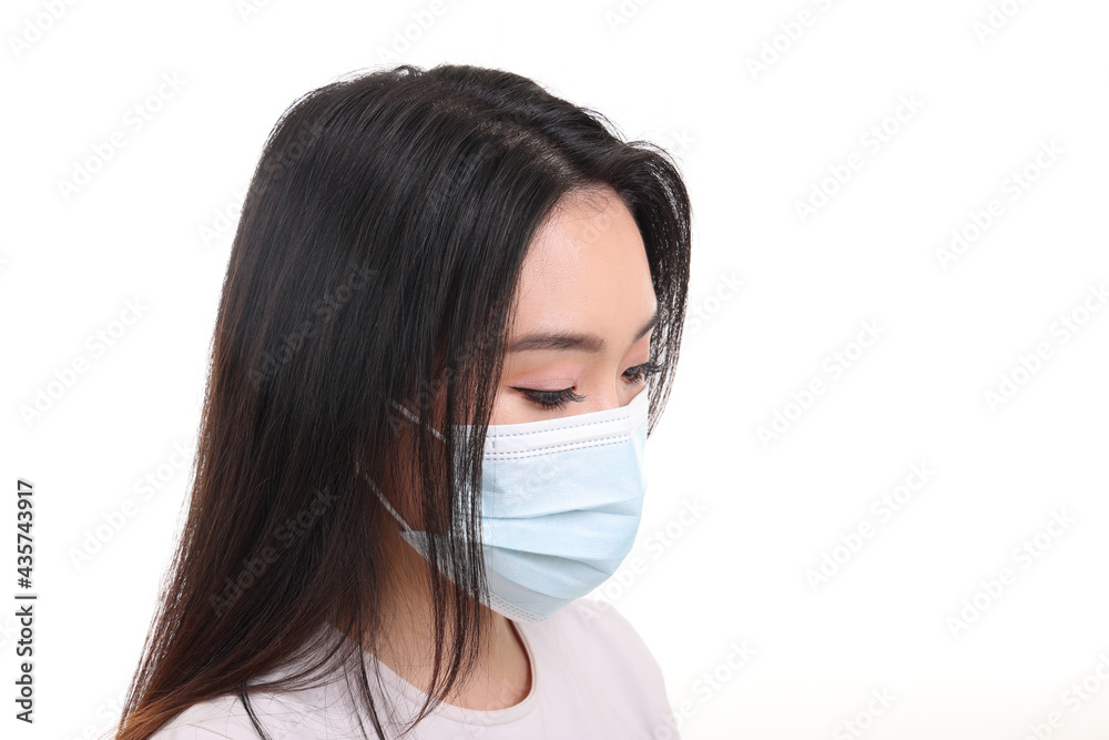 Beautiful young south east Asian woman wearing blue three ply anti virus surgical face mask on white background look down Beautiful young south east Asian woman wearing blue three ply anti virus surgical face mask on white background look down