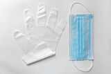 Pair of white disposable gloves and surgical face mask lie on white table in simple minimalistic composition.