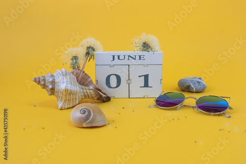 Calendar for June 1: cubes with the numbers 0 and 1, the name of the month of June in English, shells, sea stones, sunglasses, faded dandelions on a yellow background photo