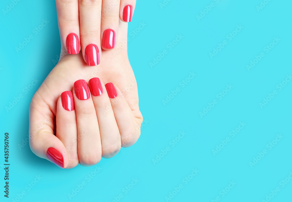 Female hands with red manicure on blue background, copy space - obrazy, fototapety, plakaty 
