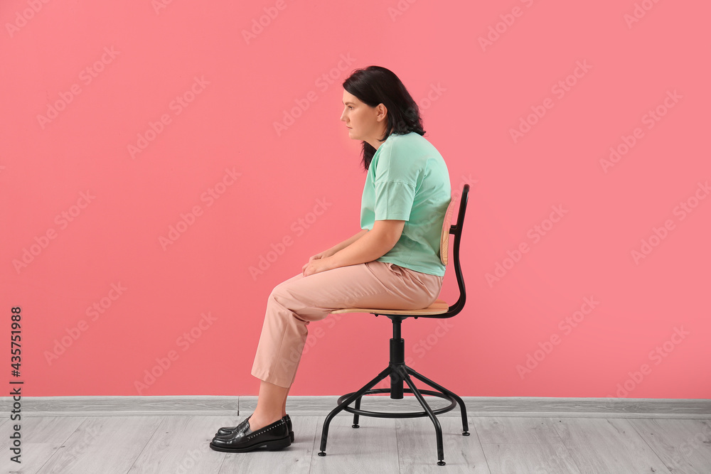 Woman with bad posture sitting on chair near color wall - obrazy, fototapety, plakaty 