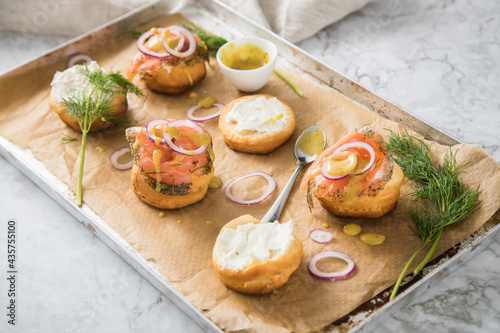 Gravlax Graved Lachs, ein roh gebeizter Fisch mit Dill auf Brötchen mit Frischkäse, Hovmästarsås Senf Soße, Zwiebelringe, auf Backblech mit Backpapier und hell Marmor Hintergrund photo