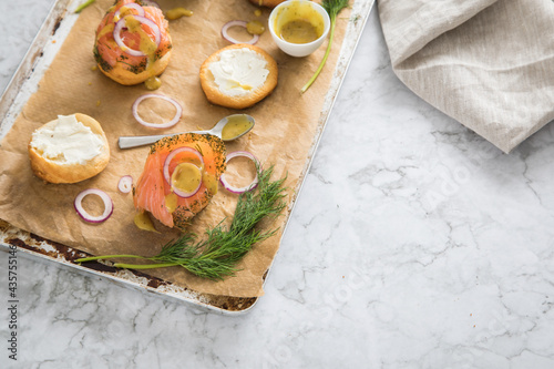 Gravlax Graved Lachs, ein roh gebeizter Fisch mit Dill auf Brötchen mit Frischkäse, Hovmästarsås Senf Soße, Zwiebelringe, auf Backblech mit Backpapier und hell Marmor Hintergrund photo