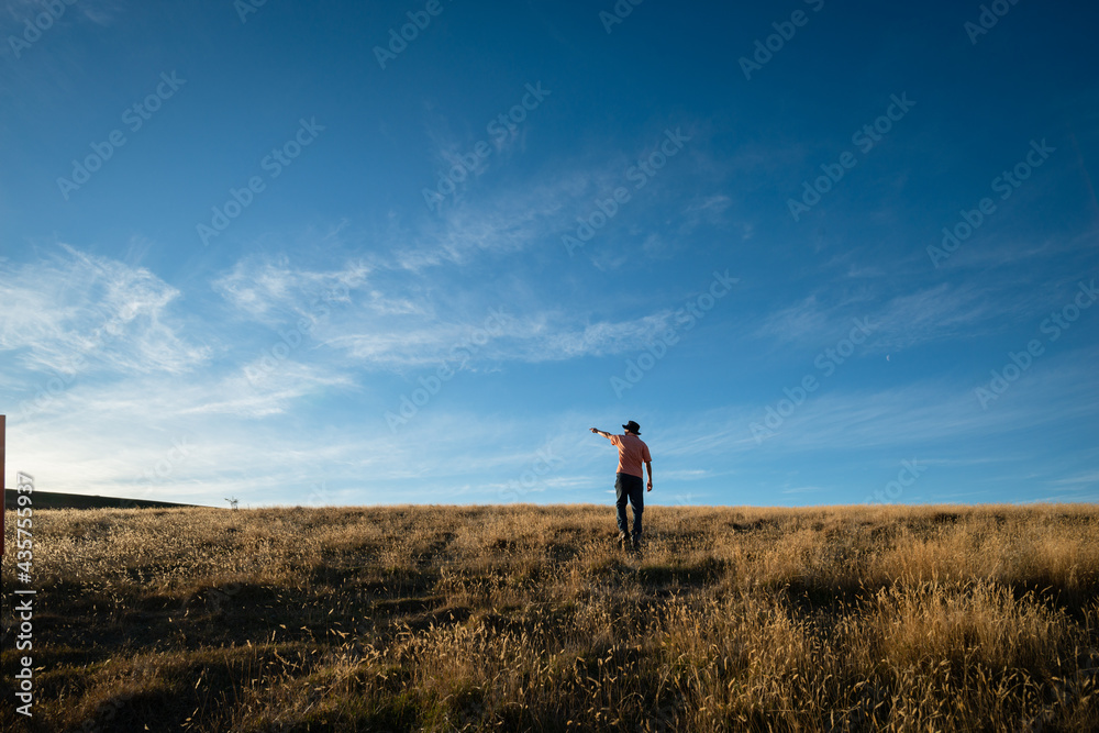 Tourist standing on the dried yellow grass and pointing at the sun, moments before sunset with a golden light