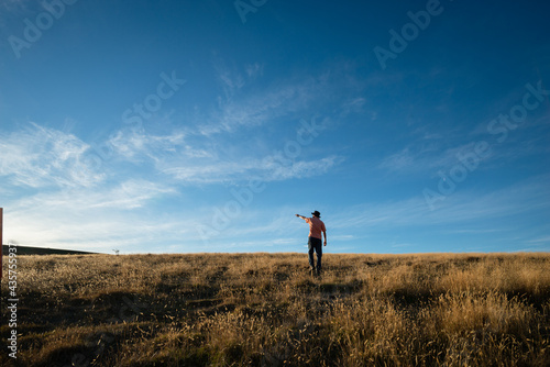 Tourist standing on the dried yellow grass and pointing at the sun, moments before sunset with a golden light