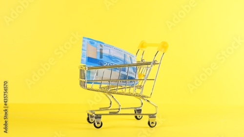 Shopping cart with 2000 rubles banknote on a yellow background, closeup. Black Friday Shopping and Discount Concept